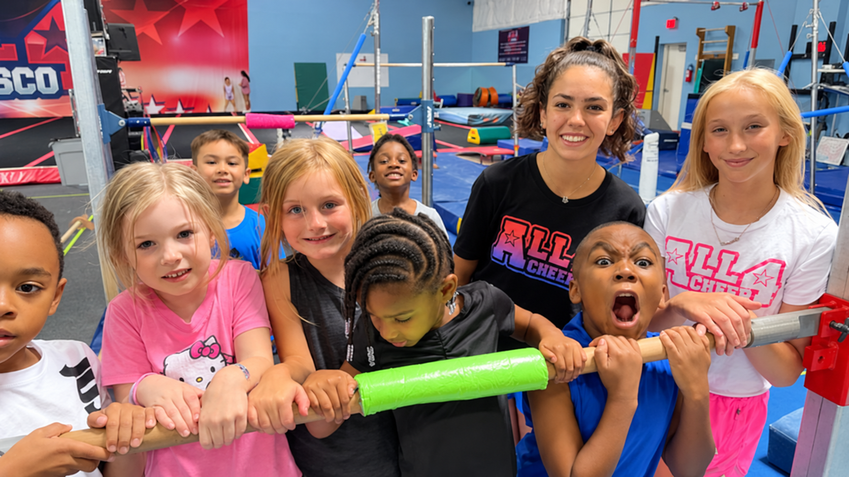 Kids and coaches laughing together while hanging on a low bar during open gym